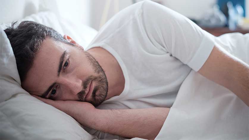 sad man laying in bed - how vicodin may be affecting your sex life