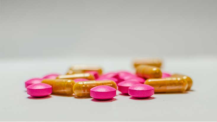 pile of pink and orange pills on a table - How Long Does Adderall Stay In Your System?