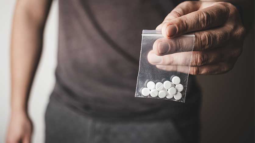 man holding a small plastic bag full of white pills - Percocet Street Names